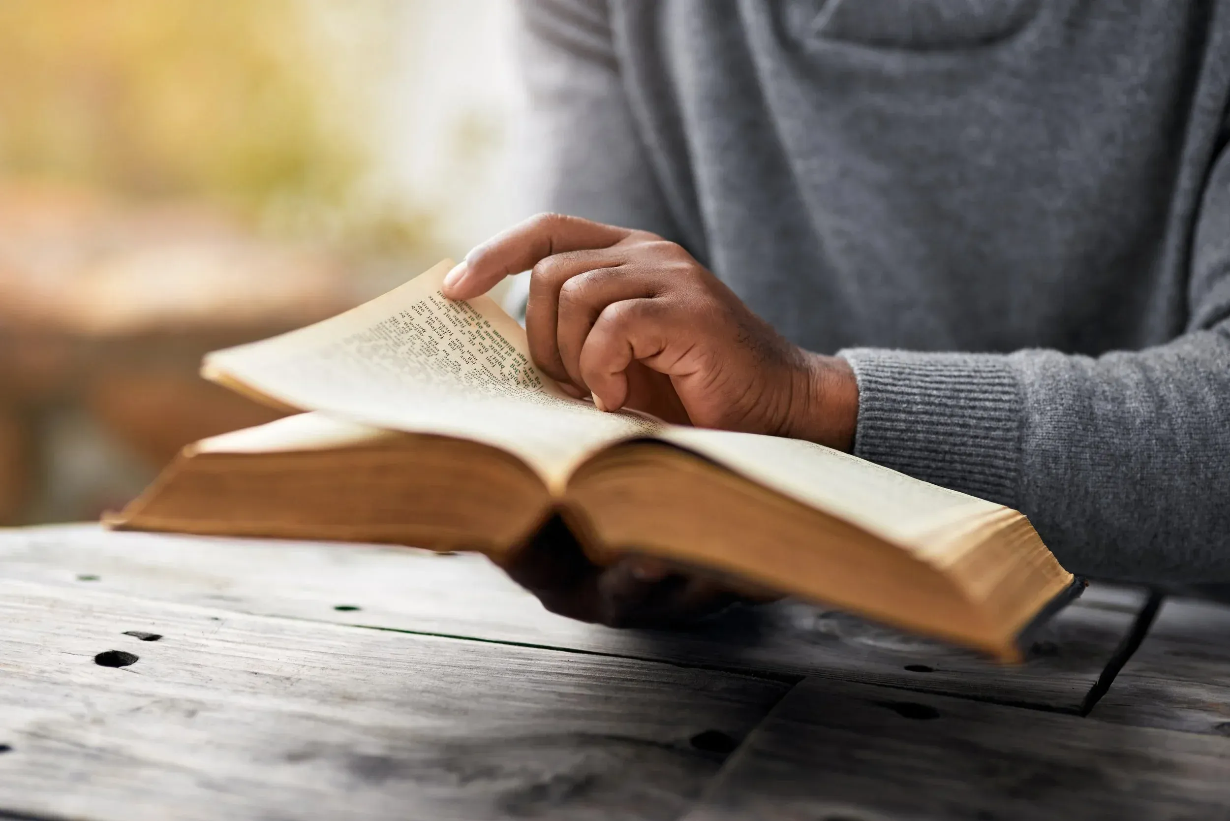 Person reading an open Bible on a wooden table outdoors.
