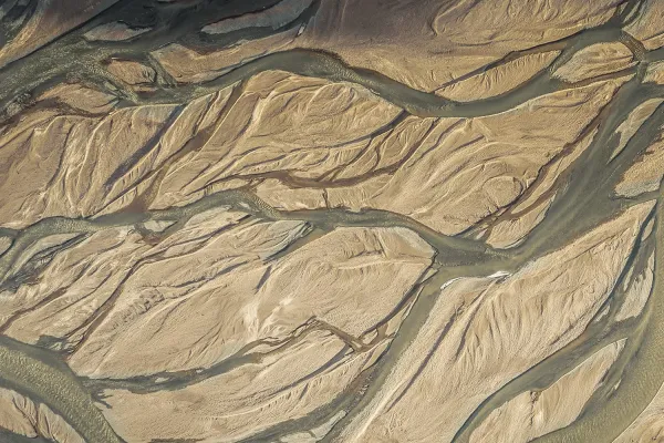 Aerial view of winding rivers and dried riverbeds in a desert landscape with tan and dark brown colors.