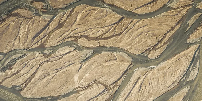 Aerial view of a river delta with multiple branching waterways and sedimentary patterns in a dry, desert-like landscape.